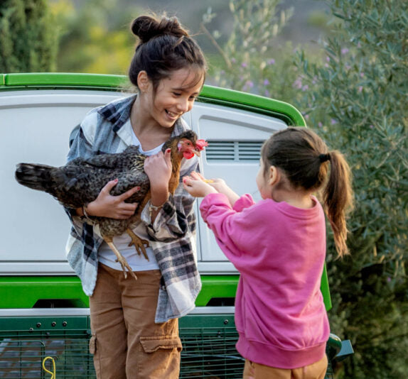 Girls holding chicken in front of coop